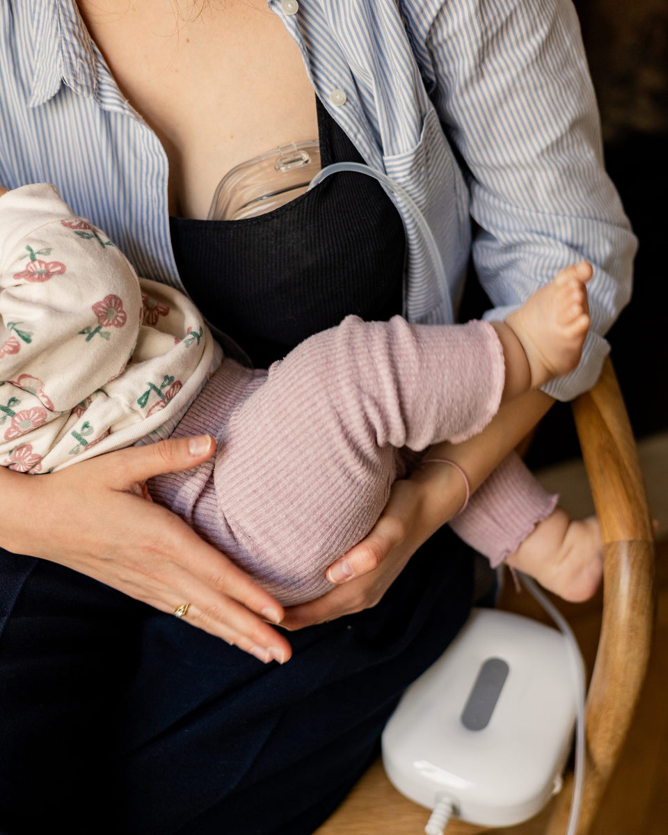 Een mama kolft met de Lileo-borstkolf, haar baby op schoot.