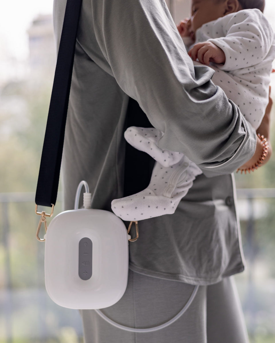 Een mama houdt haar baby vast, de Lileo-borstkolf als een tas over de schouder gedragen.